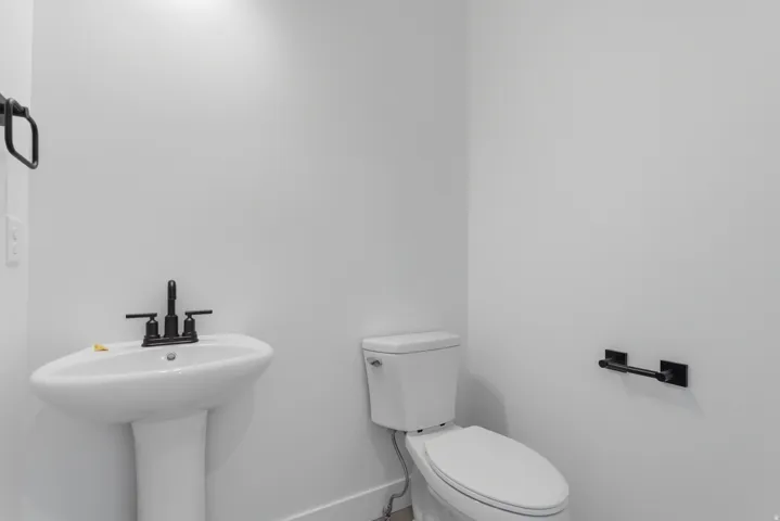 Pedestal sink with black faucet, white toilet, and matte black hardware against light-toned walls
