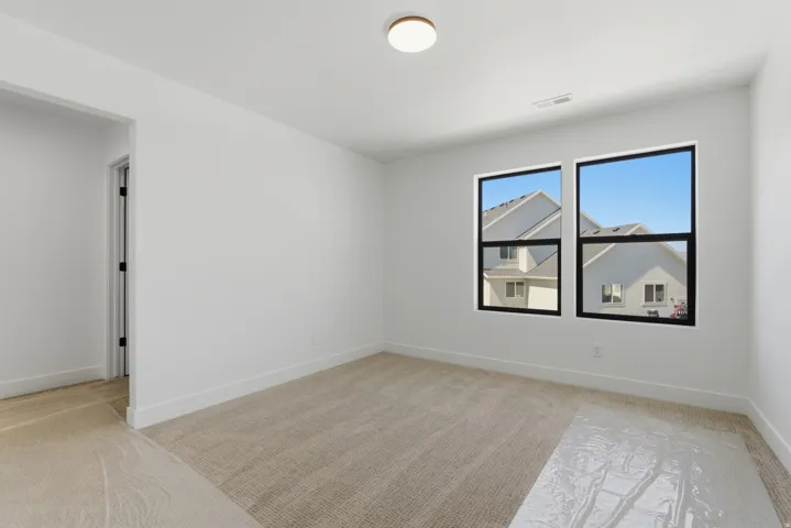 Carpeted room featuring dual windows with black frames, white walls, white baseboards, and a flush-mount ceiling light fixture