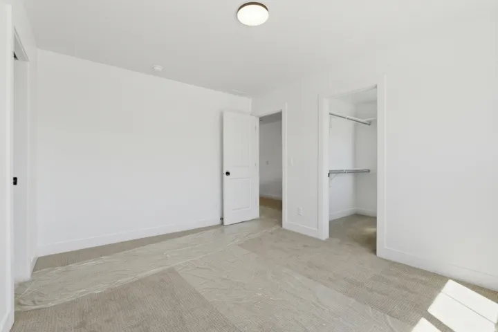 Neutral tone carpeted room with white walls, a white door with black hardware, and an open closet featuring a hanging rod and shelving