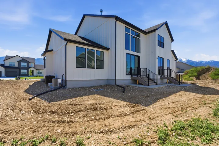 Modern farmhouse exterior featuring vertical white siding, black trim, a dark shingle roof, large black-framed windows, and two outdoor patios with black railings