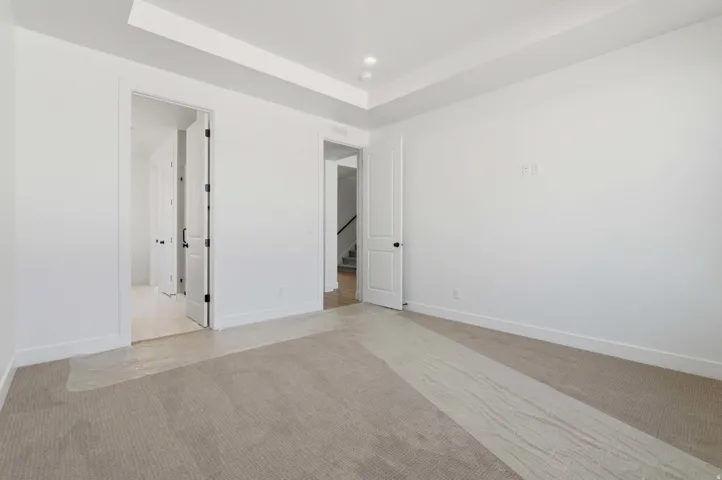 Expansive room featuring recessed lighting, a tray ceiling, light neutral carpeting, white baseboards, and a white interior door with black hardware