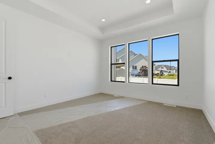 Spacious room featuring three large windows with black frames, a tray ceiling, recessed lighting, and light-toned carpeting