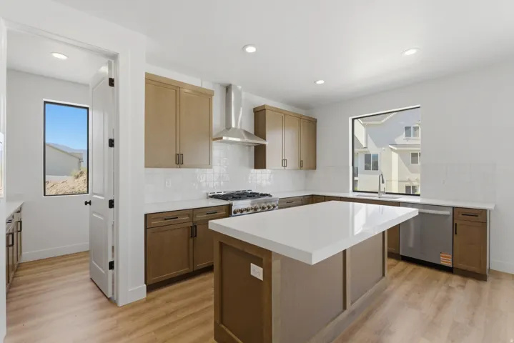 Modern kitchen featuring a central island with a solid surface countertop, wood-finish flooring, recessed lighting, and stainless steel appliances