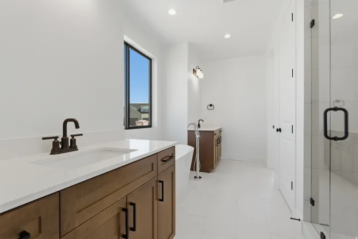 Spacious bathroom featuring dual wood-finish vanities with white countertops, a freestanding soaking tub with a floor-mounted faucet, and a glass-enclosed shower with matte black hardware
