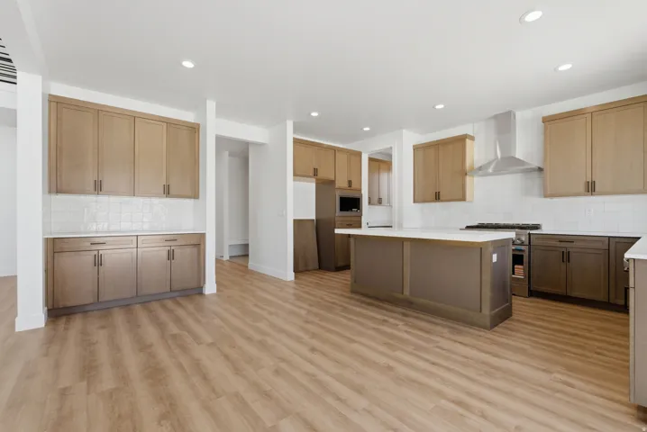 Spacious kitchen featuring an island with a white countertop, stainless steel range hood, white subway tile backsplash, recessed lighting, and wood-finish flooring