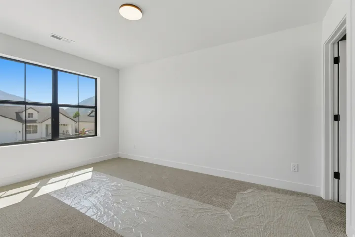 Bright interior space featuring a large black-framed window, neutral carpeting, white baseboards, and a contemporary ceiling light fixture