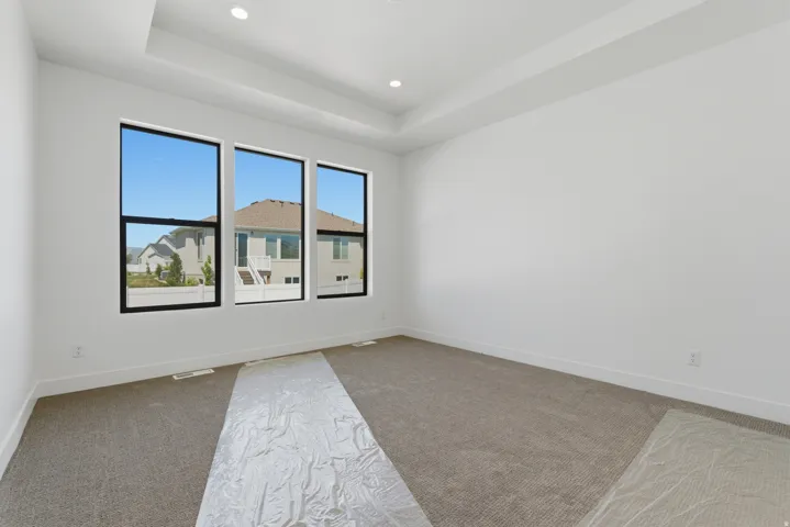 Spacious room featuring three large black-framed windows, a tray ceiling with recessed lighting, and neutral carpeting