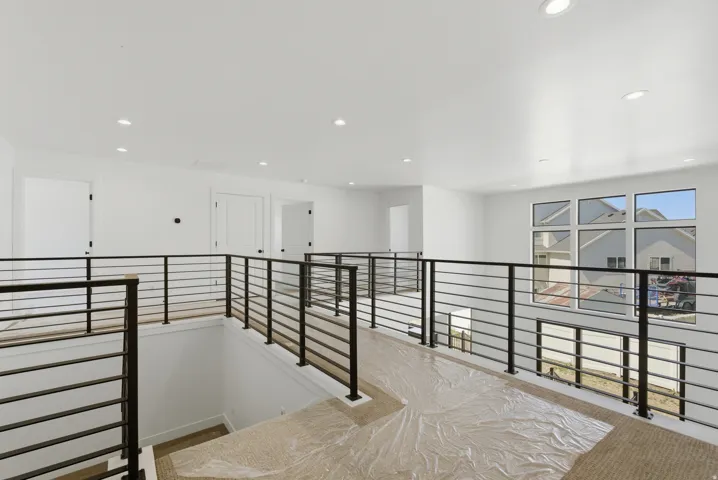 Modern loft area featuring black horizontal metal railings, recessed lighting, expansive windows, and crisp white walls