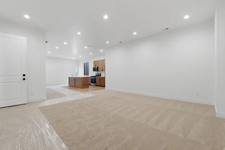 Open-concept living area featuring light-toned carpeting, recessed ceiling lighting, and crisp white walls