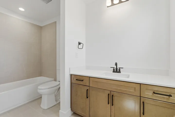 Bathroom featuring a light wood-finish vanity with a white countertop and undermount sink, a matte black faucet, and a tub with tiled surround