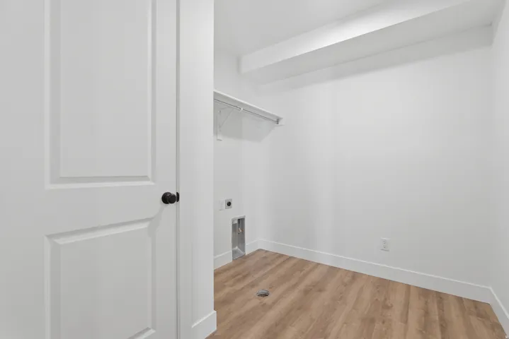Utility room featuring wood-finish flooring, white walls, and a white wire shelving unit