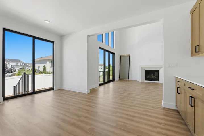 High-ceiling living space featuring wood-finish flooring, a contemporary fireplace with a white mantel, and extensive black-framed sliding glass doors