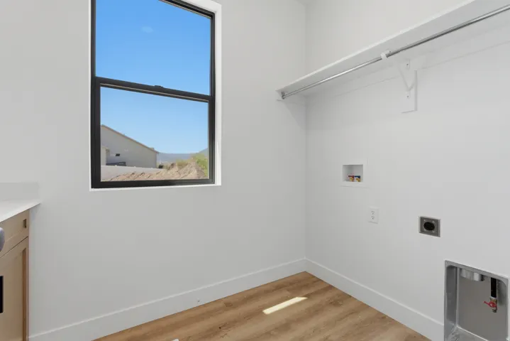 Laundry area featuring a large window with black trim, a counter with light-toned cabinetry, wood-finish flooring, a white shelf with a hanging rod, and appliance hookups
