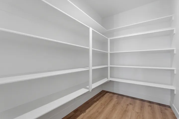 Spacious pantry featuring extensive built-in shelving, white walls, and wood-finish flooring