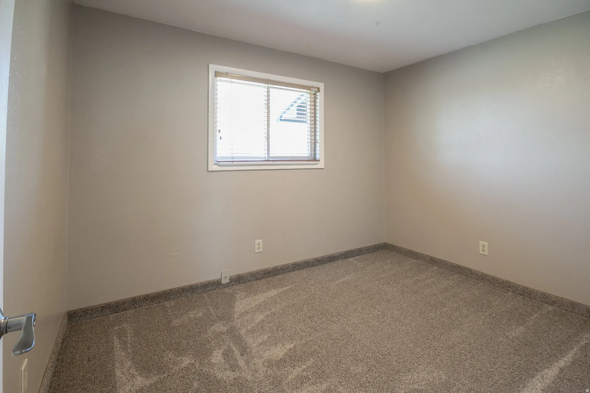 Neutral-toned room with a single window featuring horizontal blinds