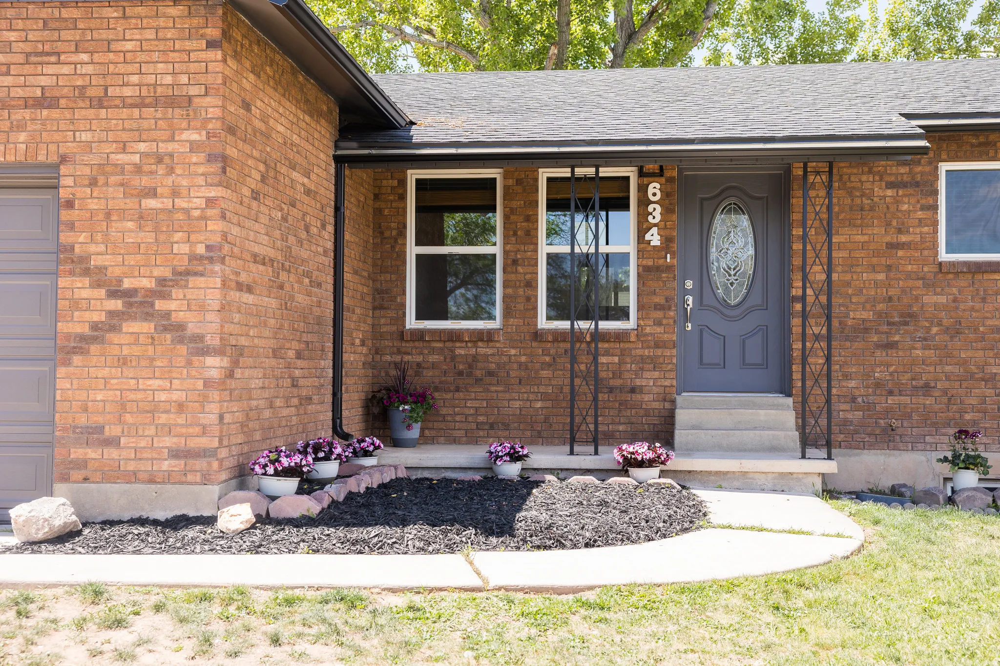 Brick exterior featuring a gray entry door with decorative glass, white-framed windows, and a covered porch
