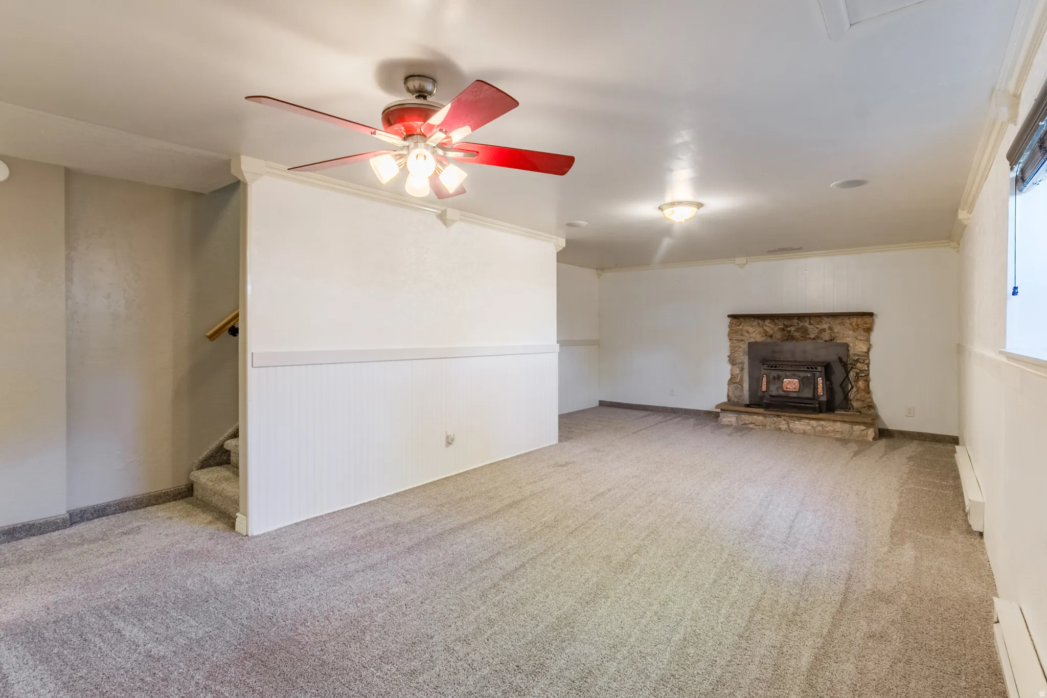 Spacious room featuring light gray carpet flooring, white beadboard wainscoting, and a stone-clad fireplace with an insert
