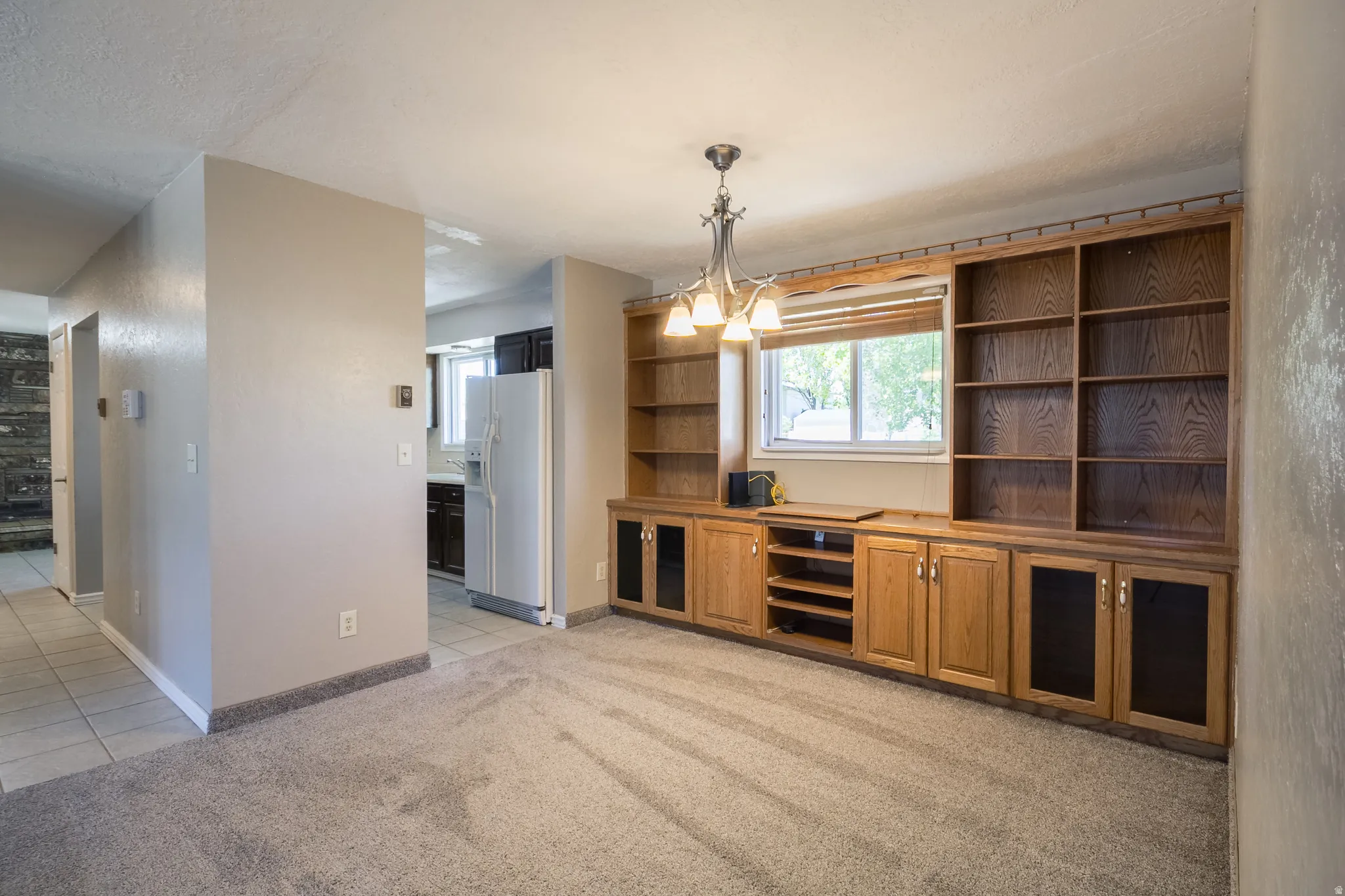 Built-in wood cabinetry with shelving and display storage frames a window, illuminated by a multi-bulb chandelier
