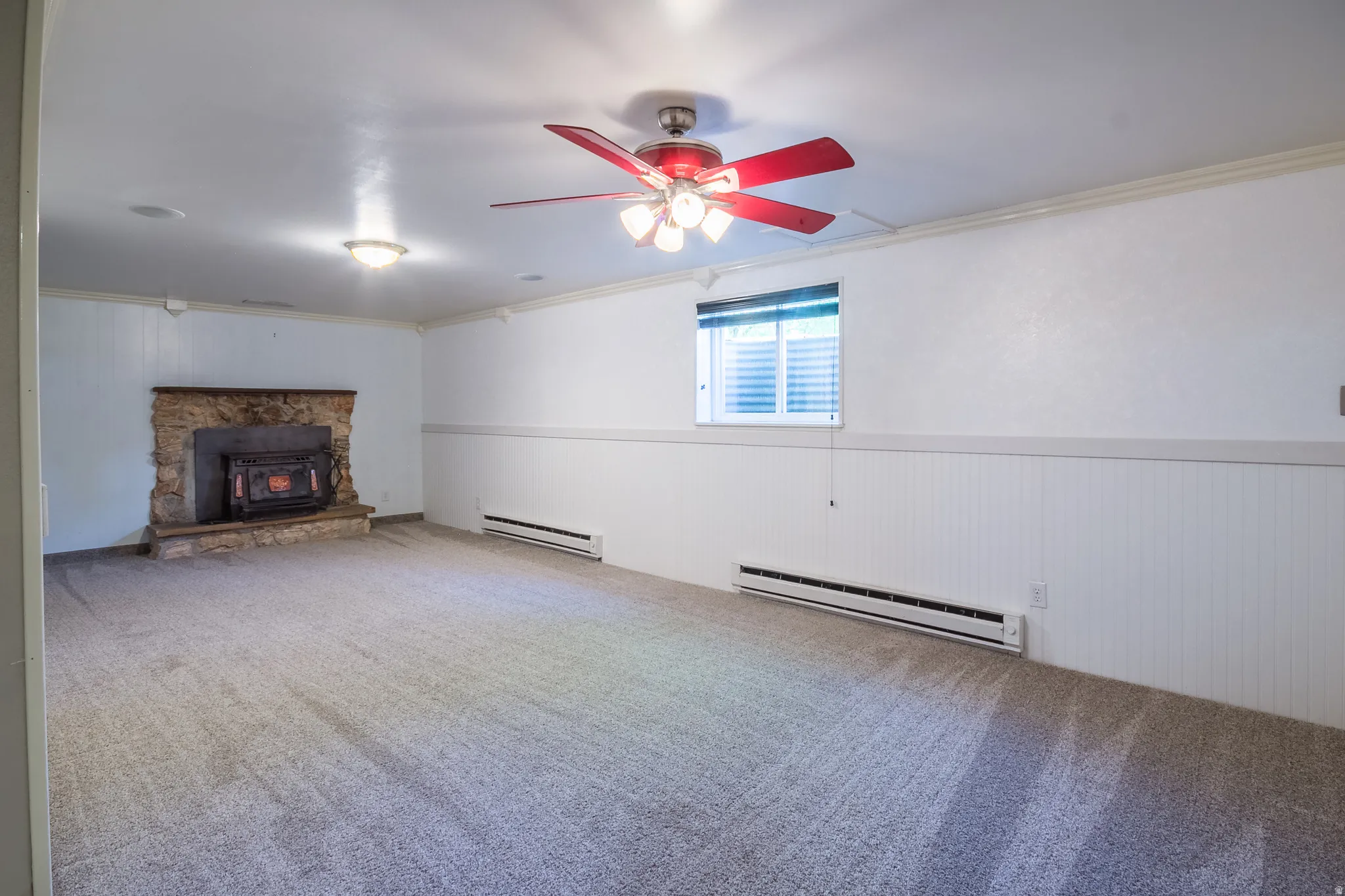 Spacious room featuring neutral carpet flooring, white beadboard wainscoting, and a stone hearth with an insert