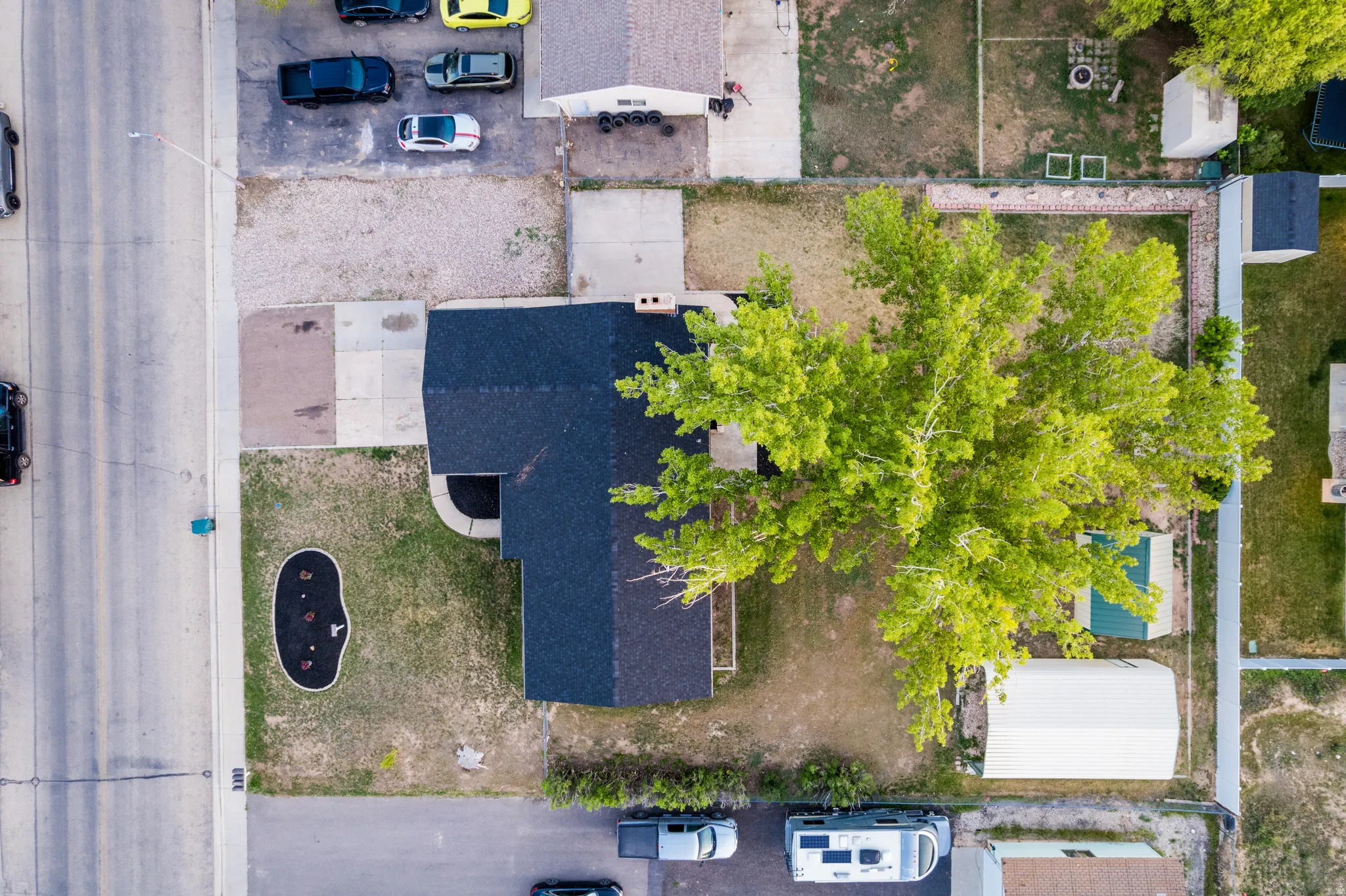 Overhead property view featuring a residence with a dark shingle roof, a paved driveway, and a large, mature tree providing ample shade