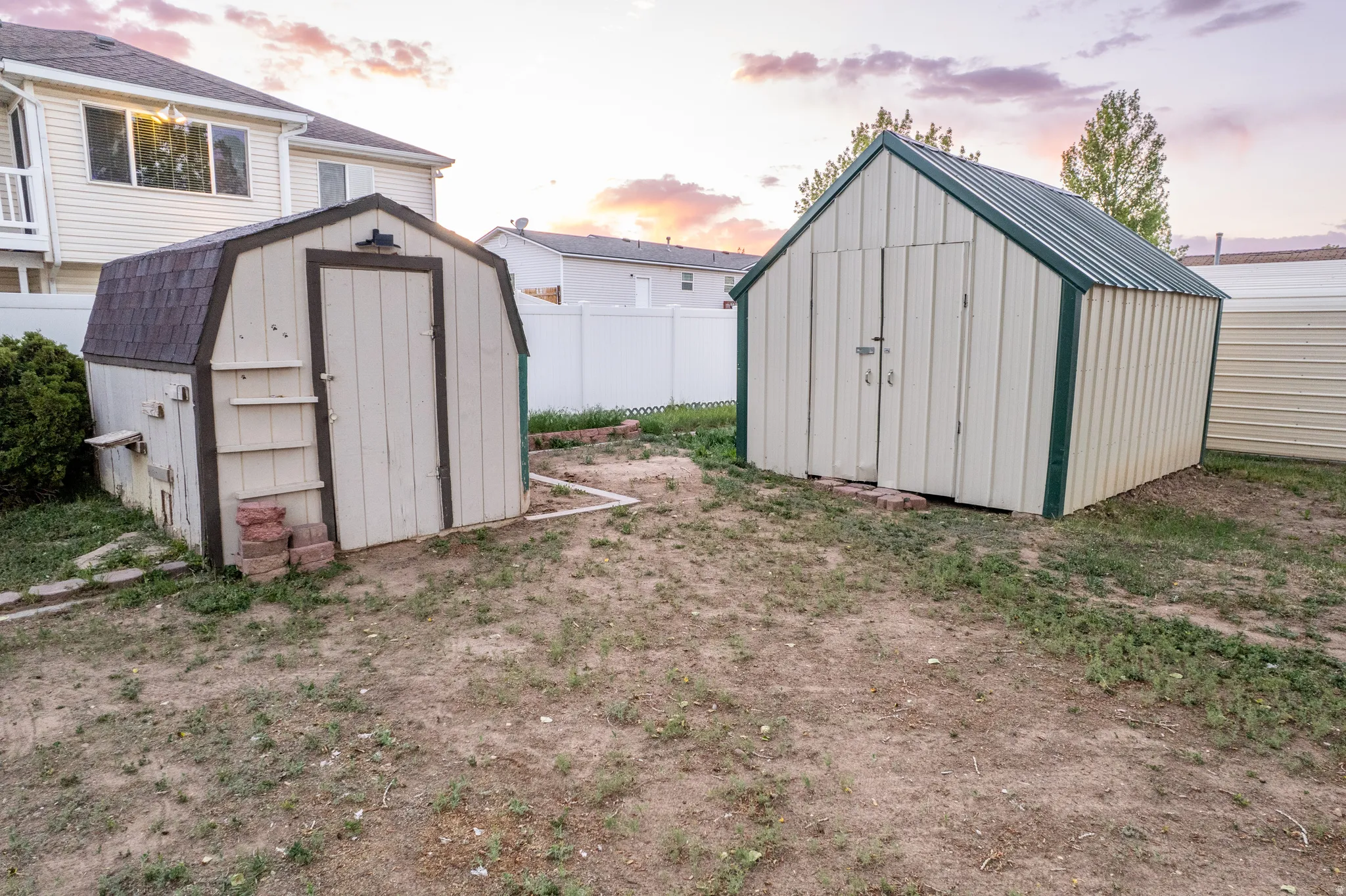 Expansive backyard area featuring two detached storage sheds, a privacy fence, and partial views of the main residence with a balcony
