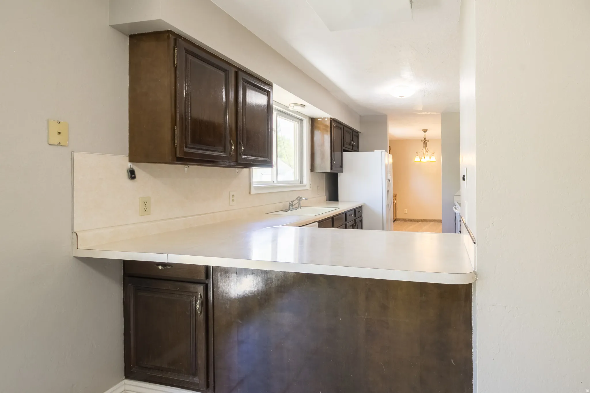 Kitchen featuring dark wood cabinetry, light-toned countertops, and a white sink with a window above