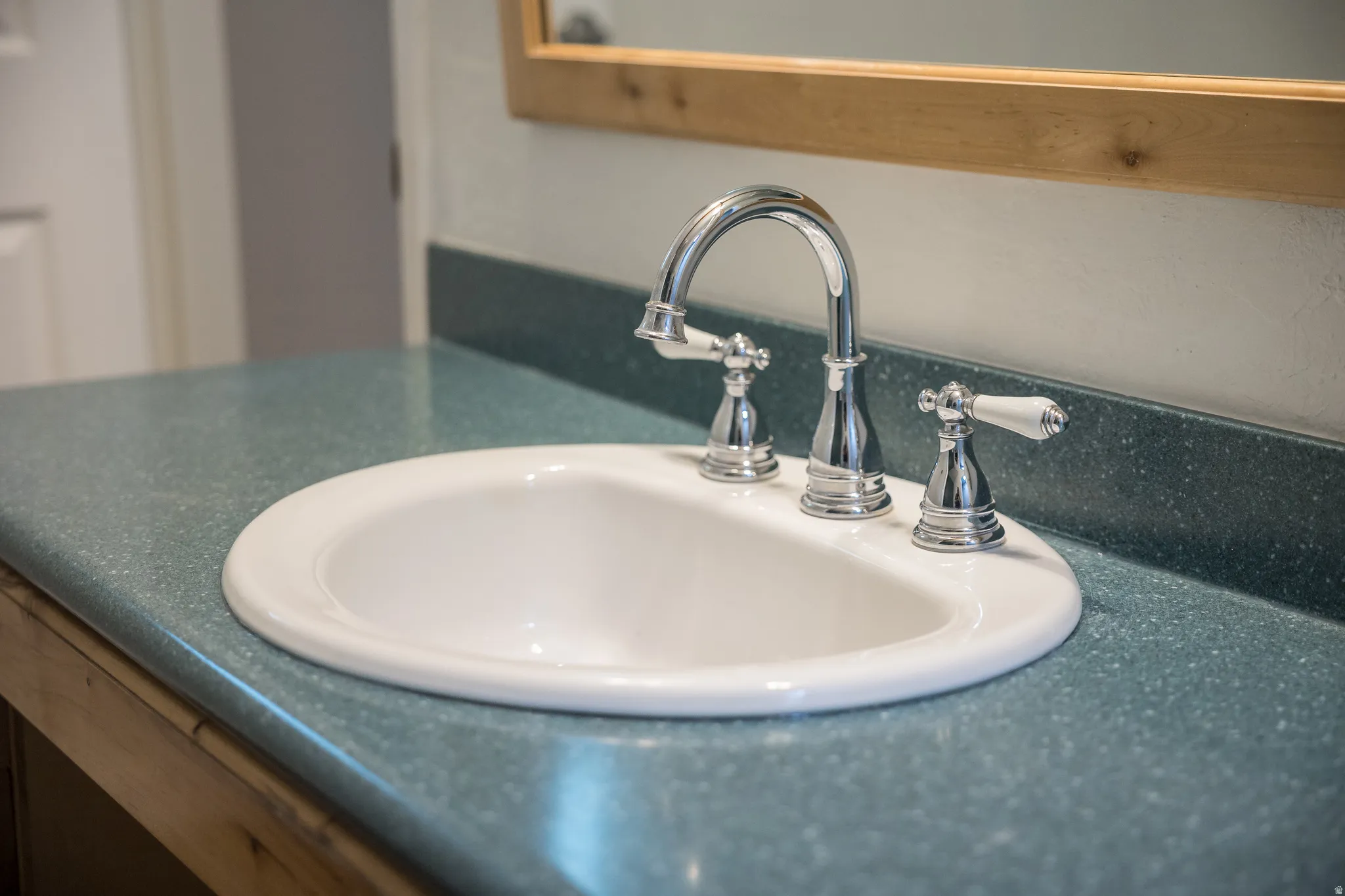 Integrated white oval sink with a chrome three-piece faucet set featuring white porcelain handles, set into a speckled turquoise countertop with a matching backsplash