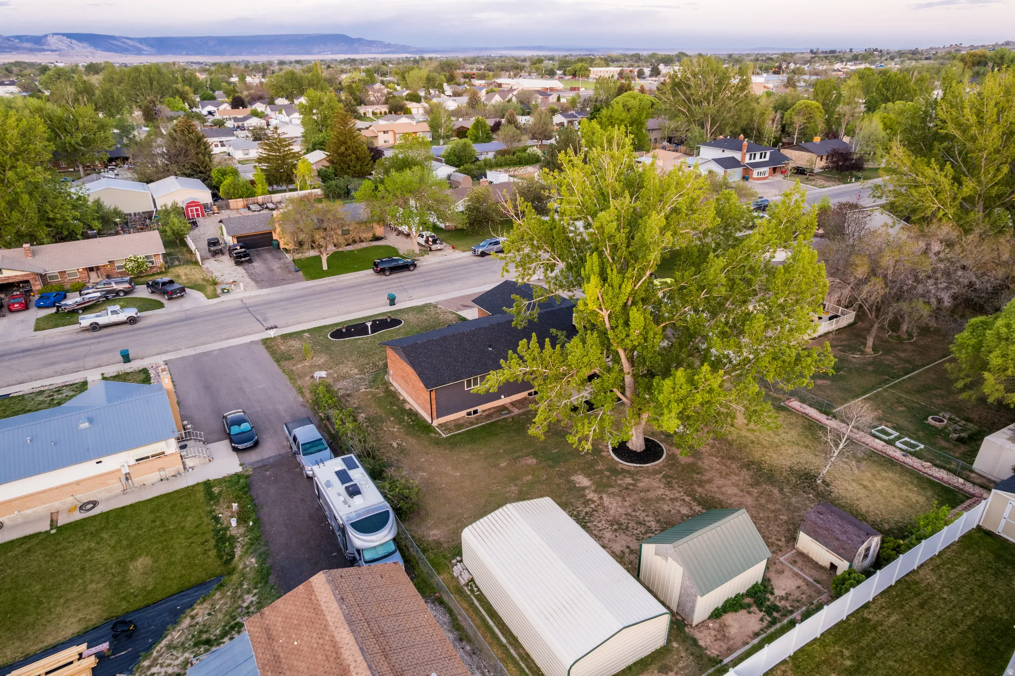 Expansive property featuring a mature shade tree, a brick and siding exterior, a dark shingled roof, and a large white vinyl fence