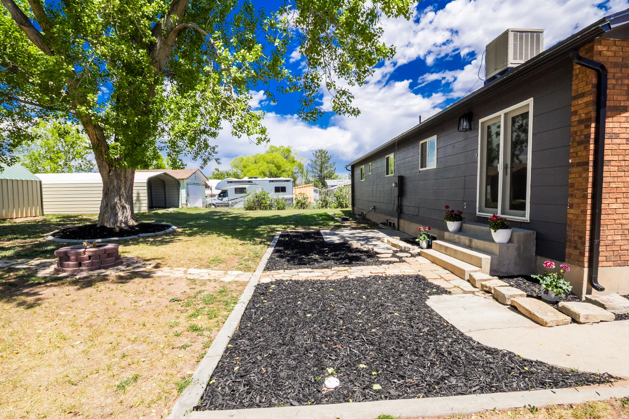 Expansive backyard featuring a mature tree, brick-ringed fire pit, and a patio with concrete steps