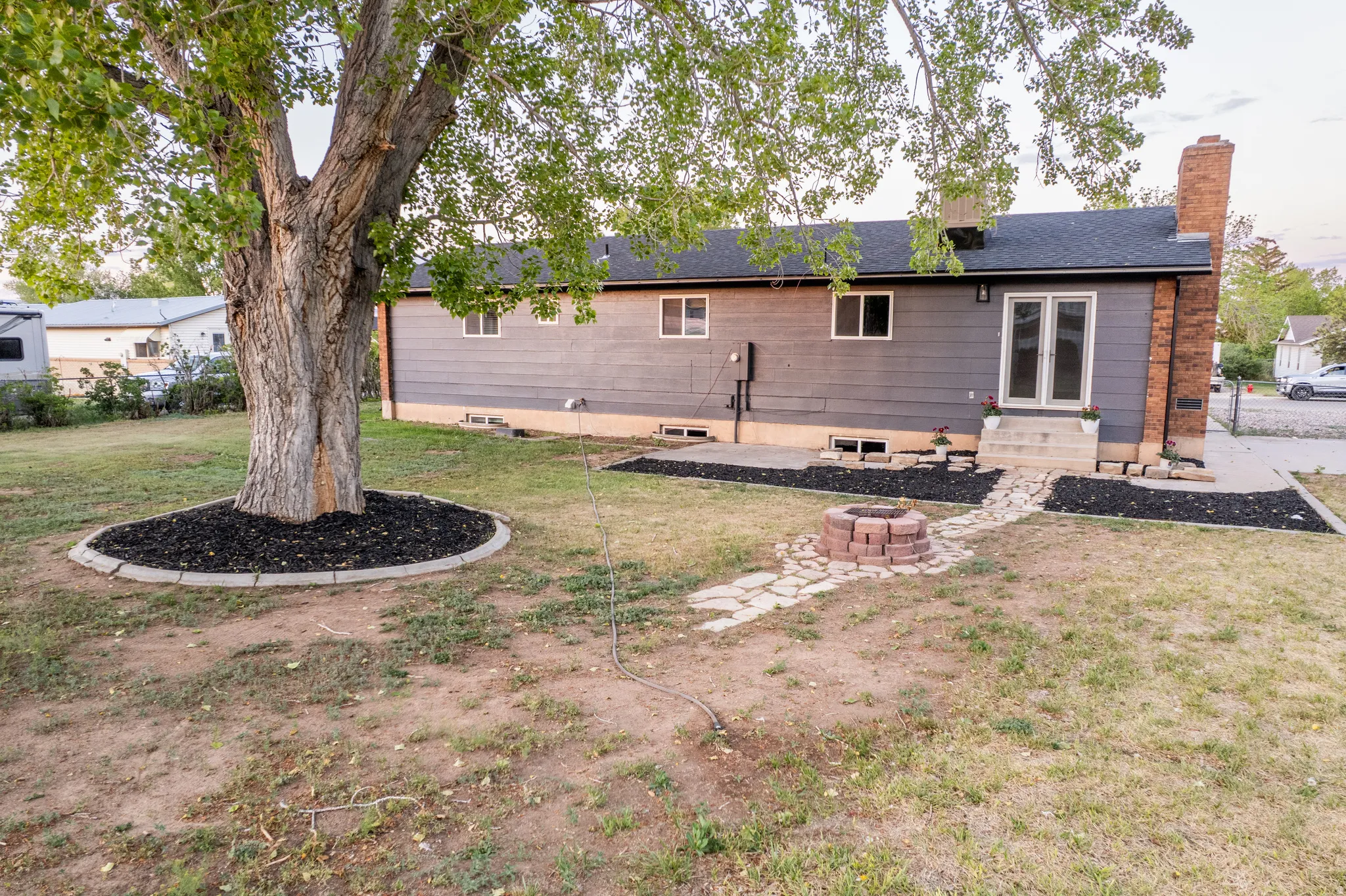 Spacious backyard featuring a large tree with a decorative mulch ring, a stone fire pit, and a flagstone pathway