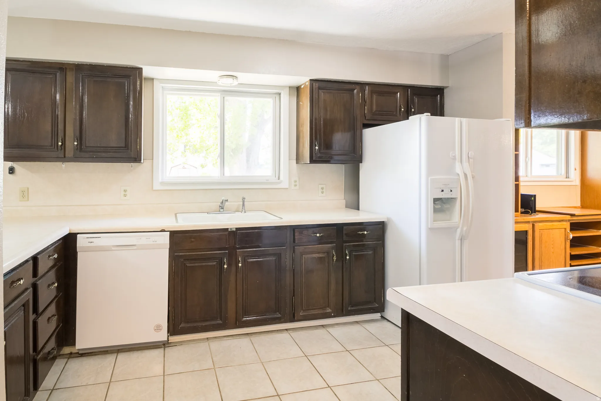 Kitchen featuring dark wood cabinetry, white countertops, a double basin sink, and a white dishwasher