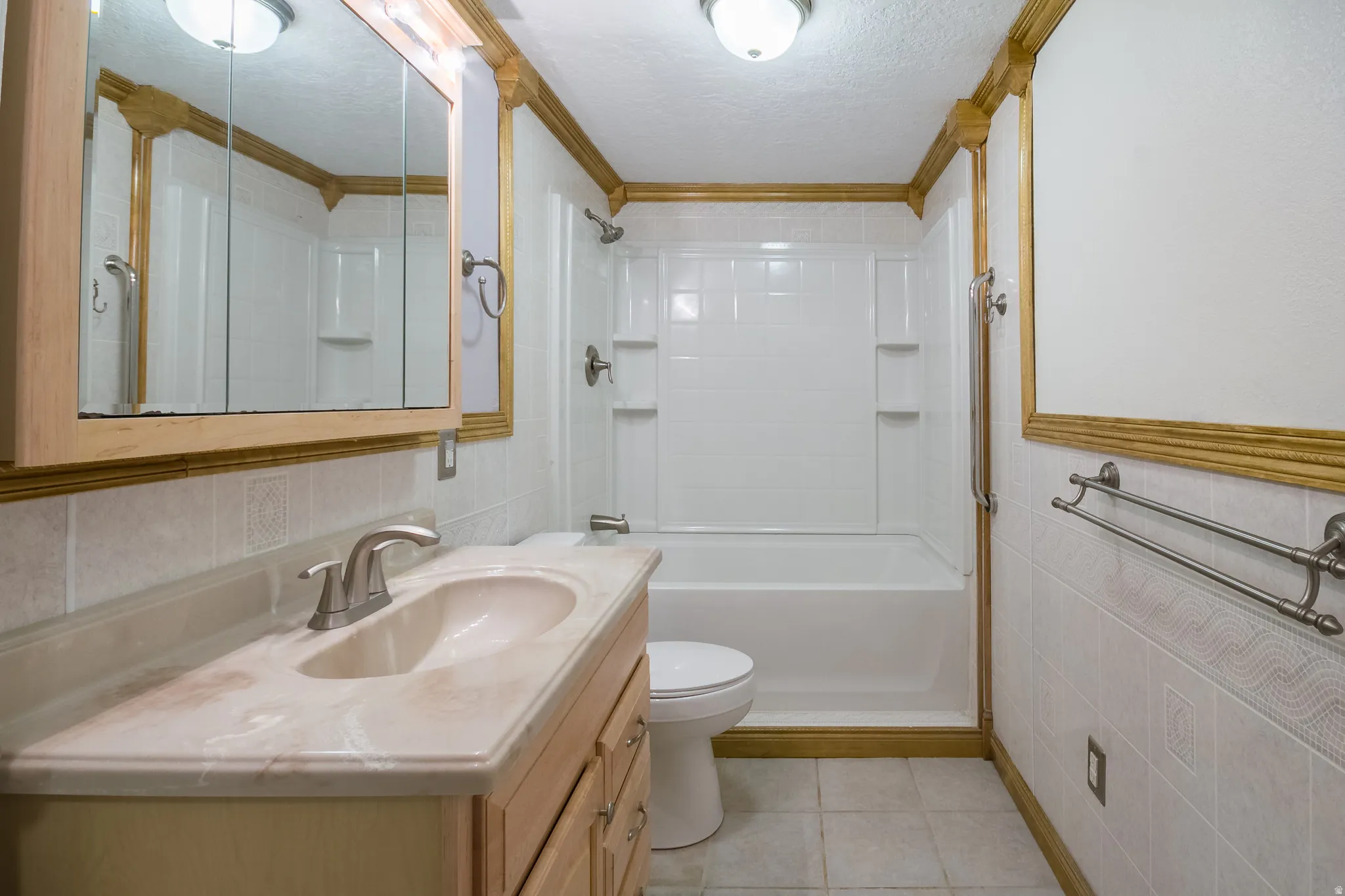 Bathroom featuring a vanity with an integrated sink, a medicine cabinet, a full bathtub with shower, and tiled walls and flooring