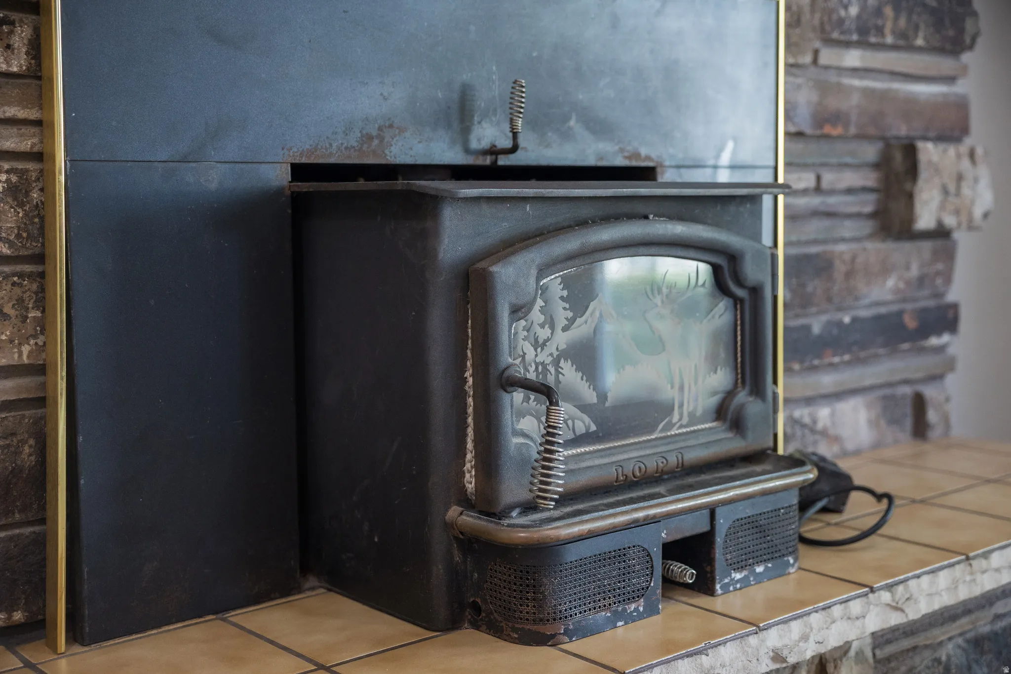 Black cast iron wood-burning stove with an etched glass door, set on a tiled hearth