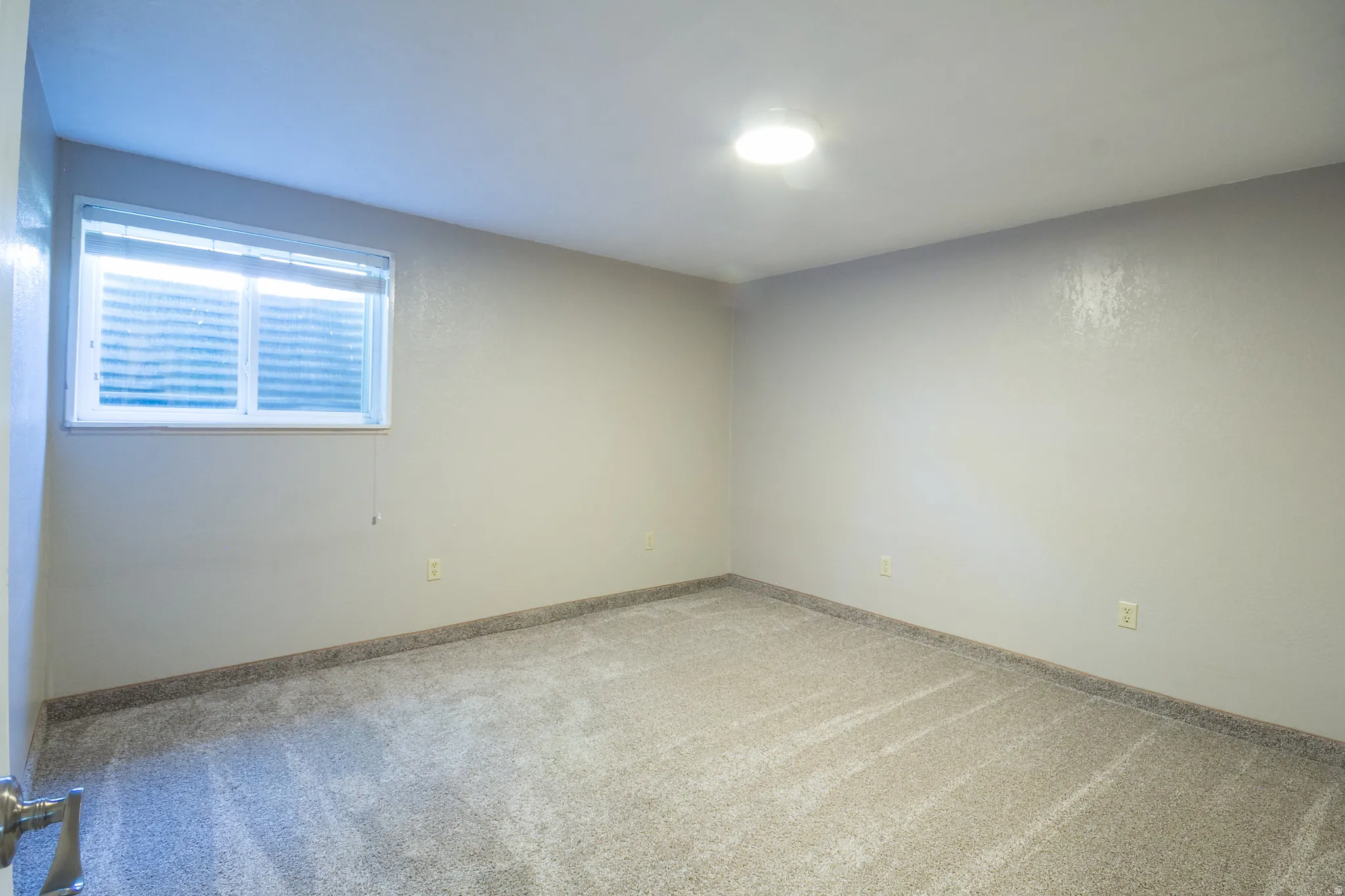 Neutral-toned room featuring a single window with horizontal blinds, light beige walls, and wall-to-wall carpeting