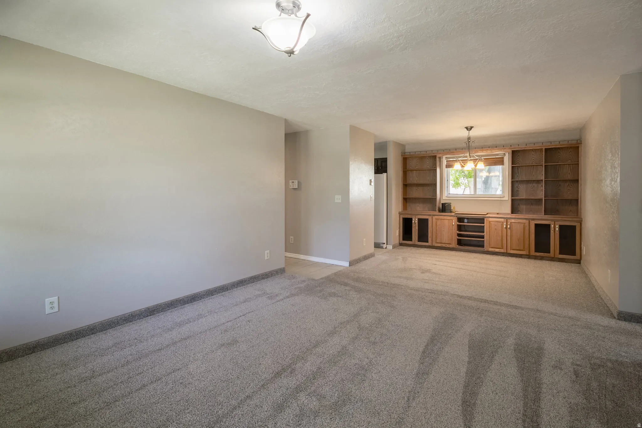 Built-in oak shelving and cabinetry with central window, overhead chandelier, and light gray carpet flooring