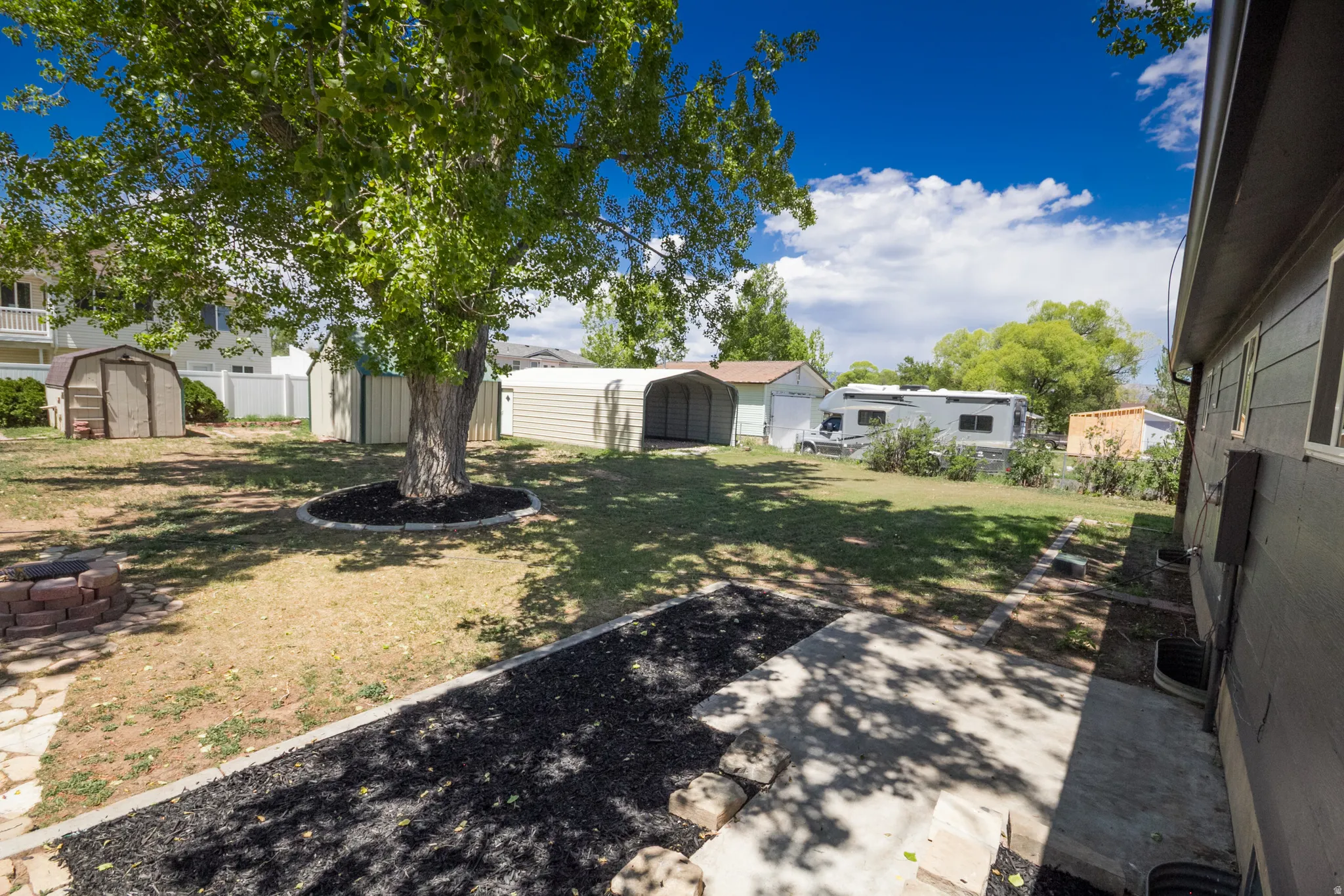 Expansive backyard featuring a mature central tree, a brick fire pit, and a concrete patio area