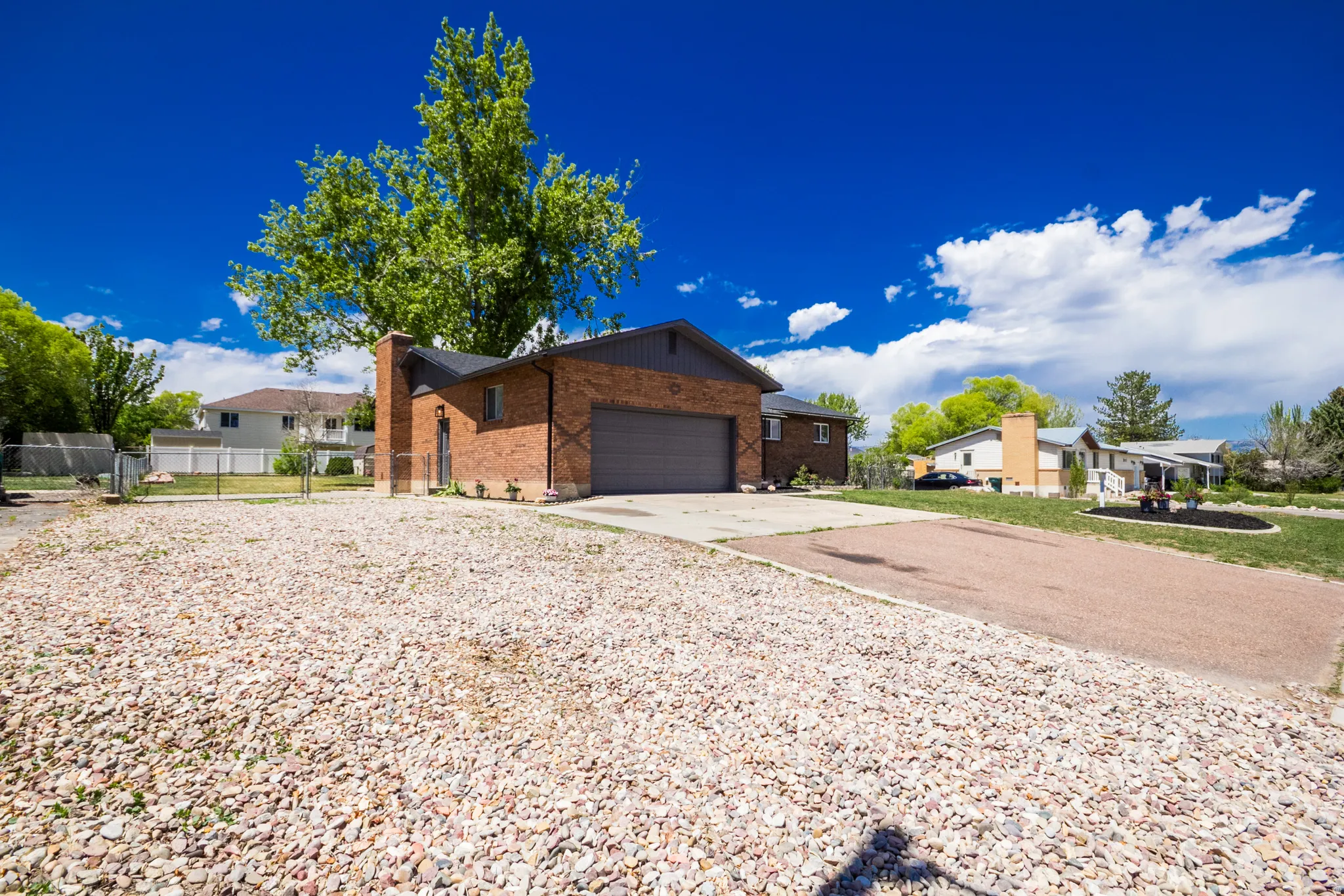Brick exterior home with an attached garage, featuring a prominent chimney structure and mature landscaping