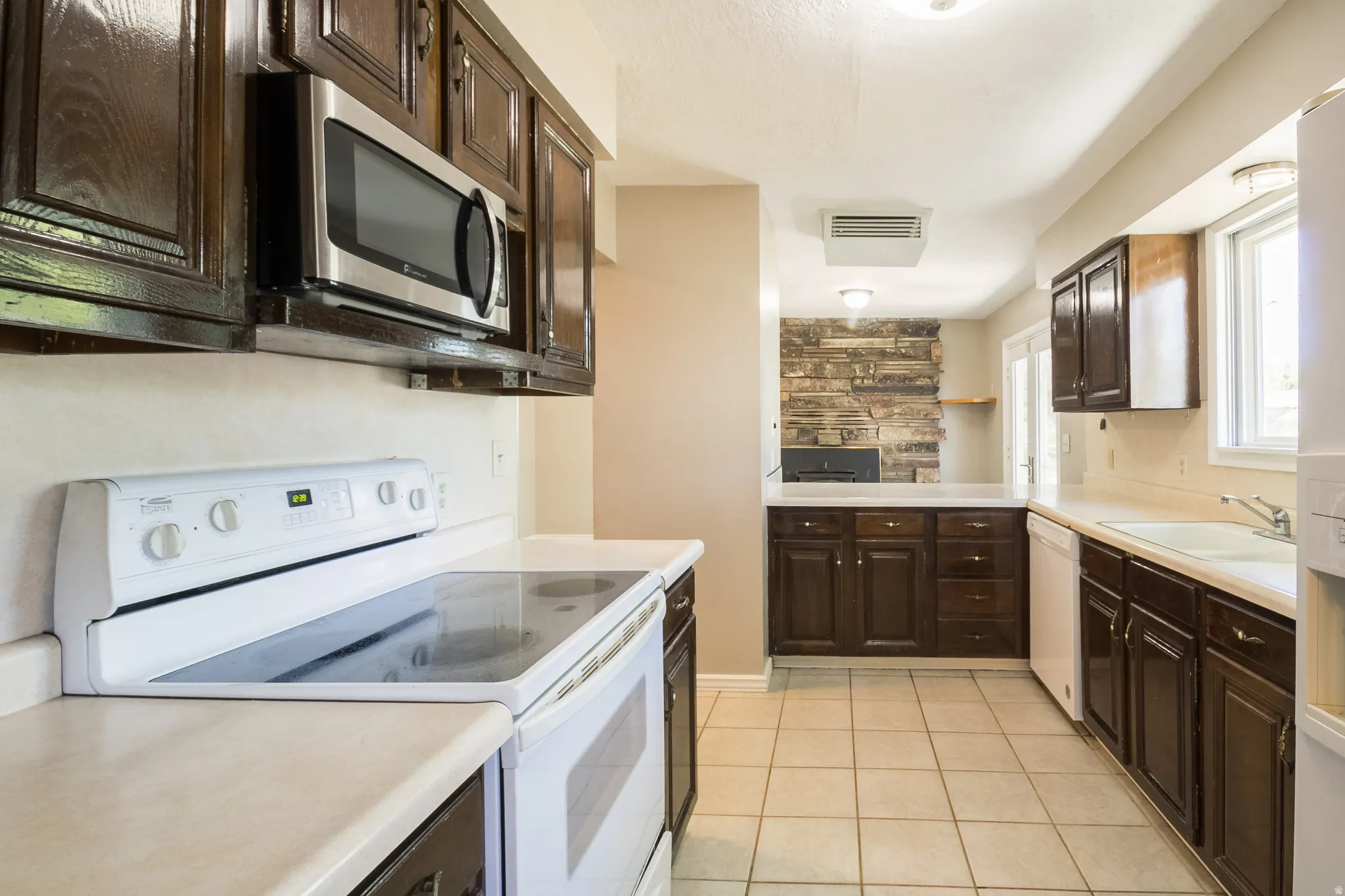 Kitchen featuring wood cabinetry, light-toned countertops, and a white electric range with an overhead stainless steel microwave