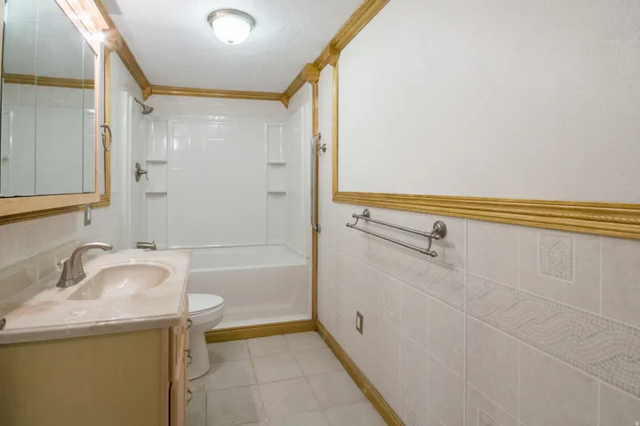 Full bathroom featuring a single vanity with an integrated sink, a built-in bathtub with shower, and decorative wall tiling