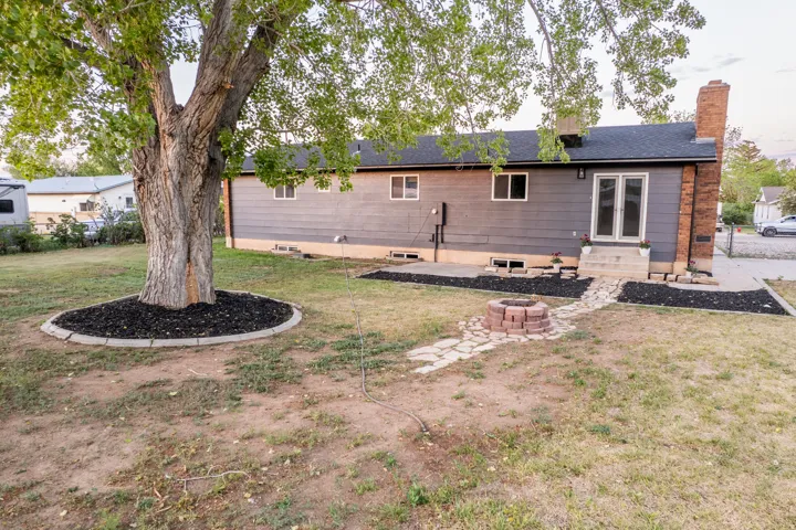 Spacious backyard featuring a large tree with a decorative mulch ring, a stone fire pit, and a flagstone pathway