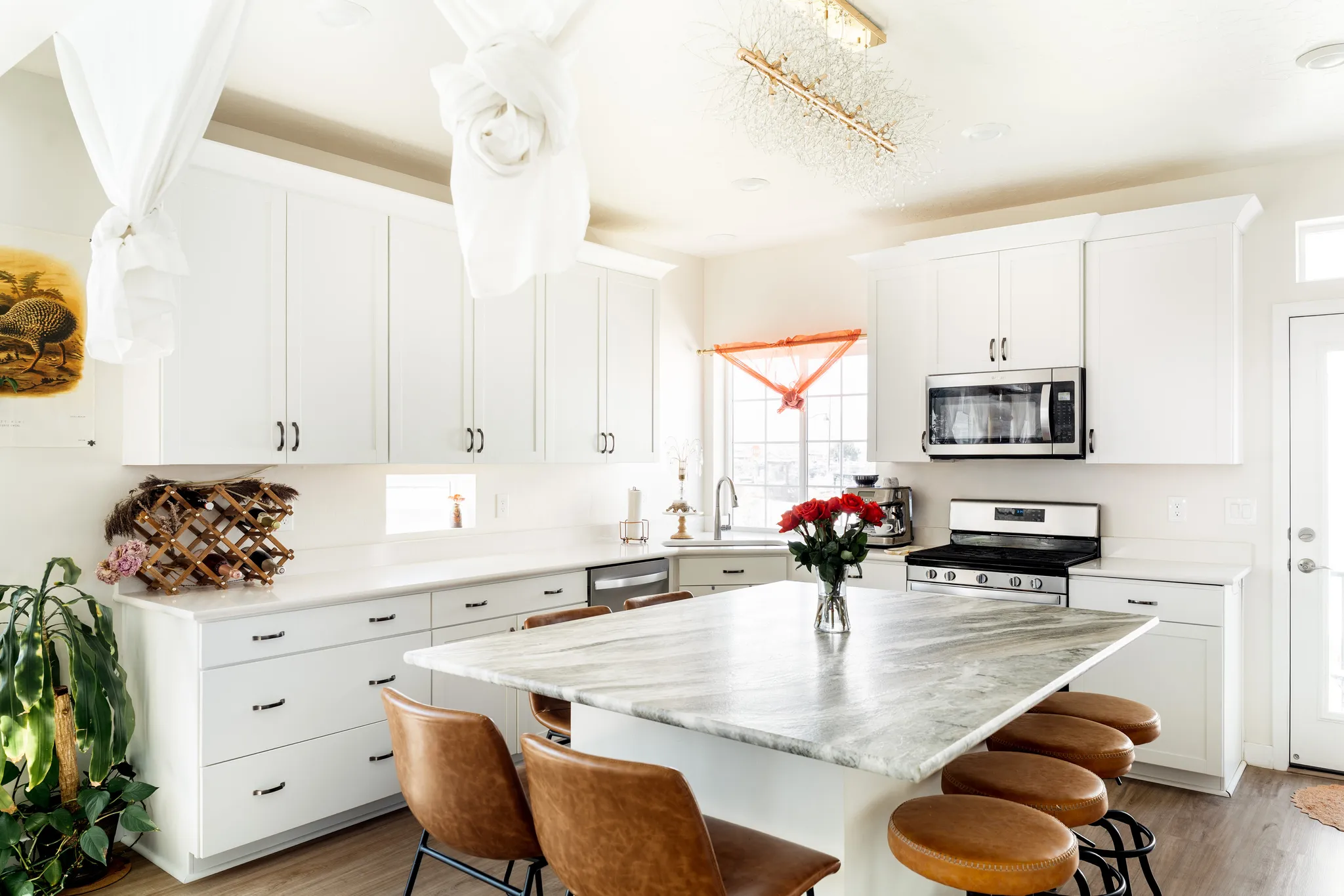 Bright kitchen featuring a central island with a stone countertop, white cabinetry with dark hardware, stainless steel appliances, and wood-finish flooring