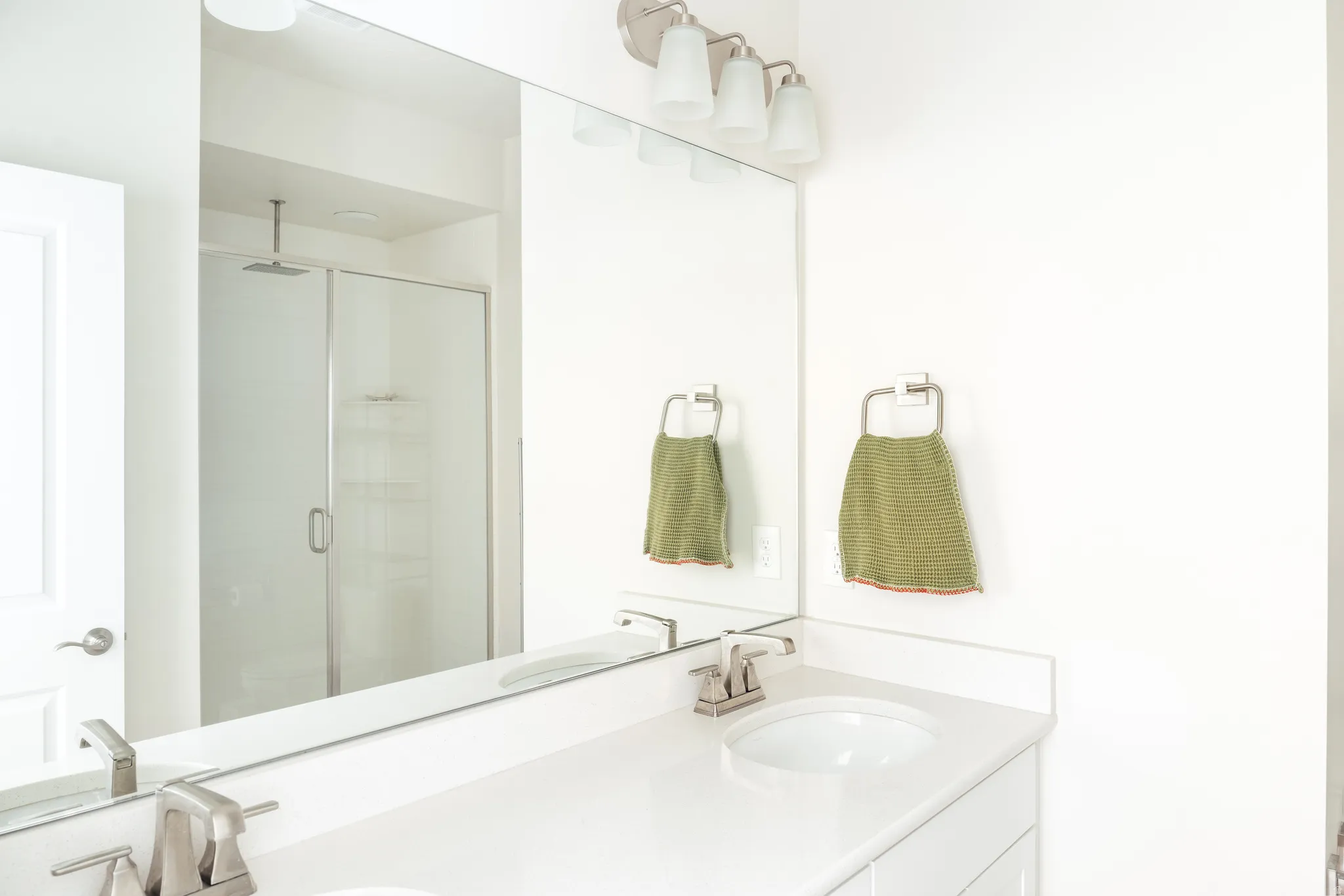 Bathroom featuring a white vanity with an integrated sink, brushed nickel faucet, large wall-mounted mirror, and a glass-enclosed shower with a rain shower head