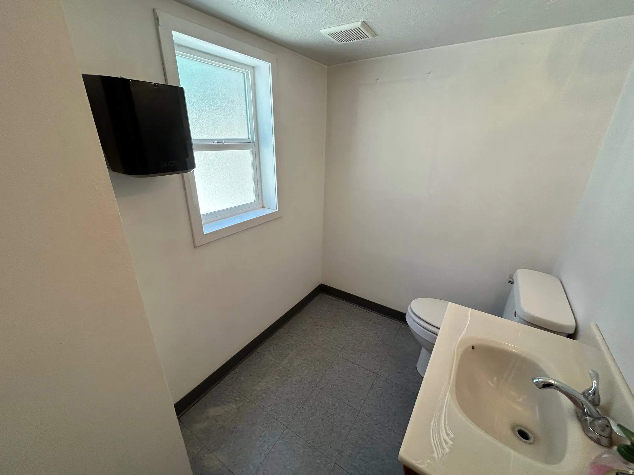 Powder room featuring a ceramic pedestal sink with a chrome faucet, a white toilet, and a window with frosted glass