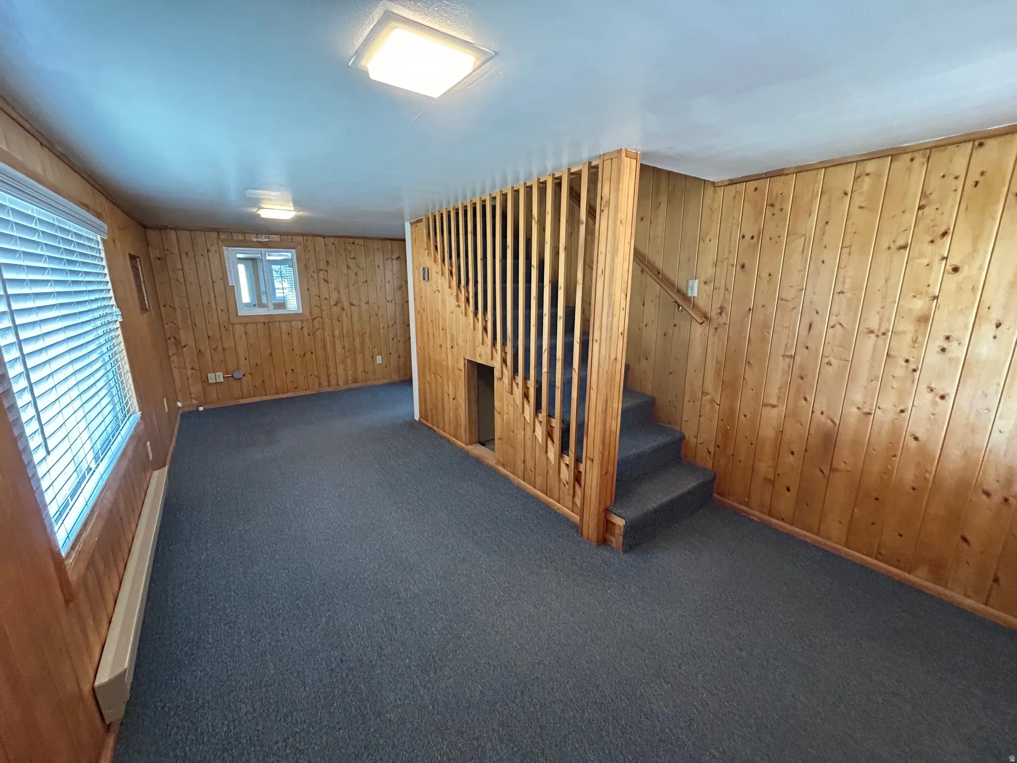 Carpeted room featuring wood paneling, a staircase with wood railing, and multiple windows