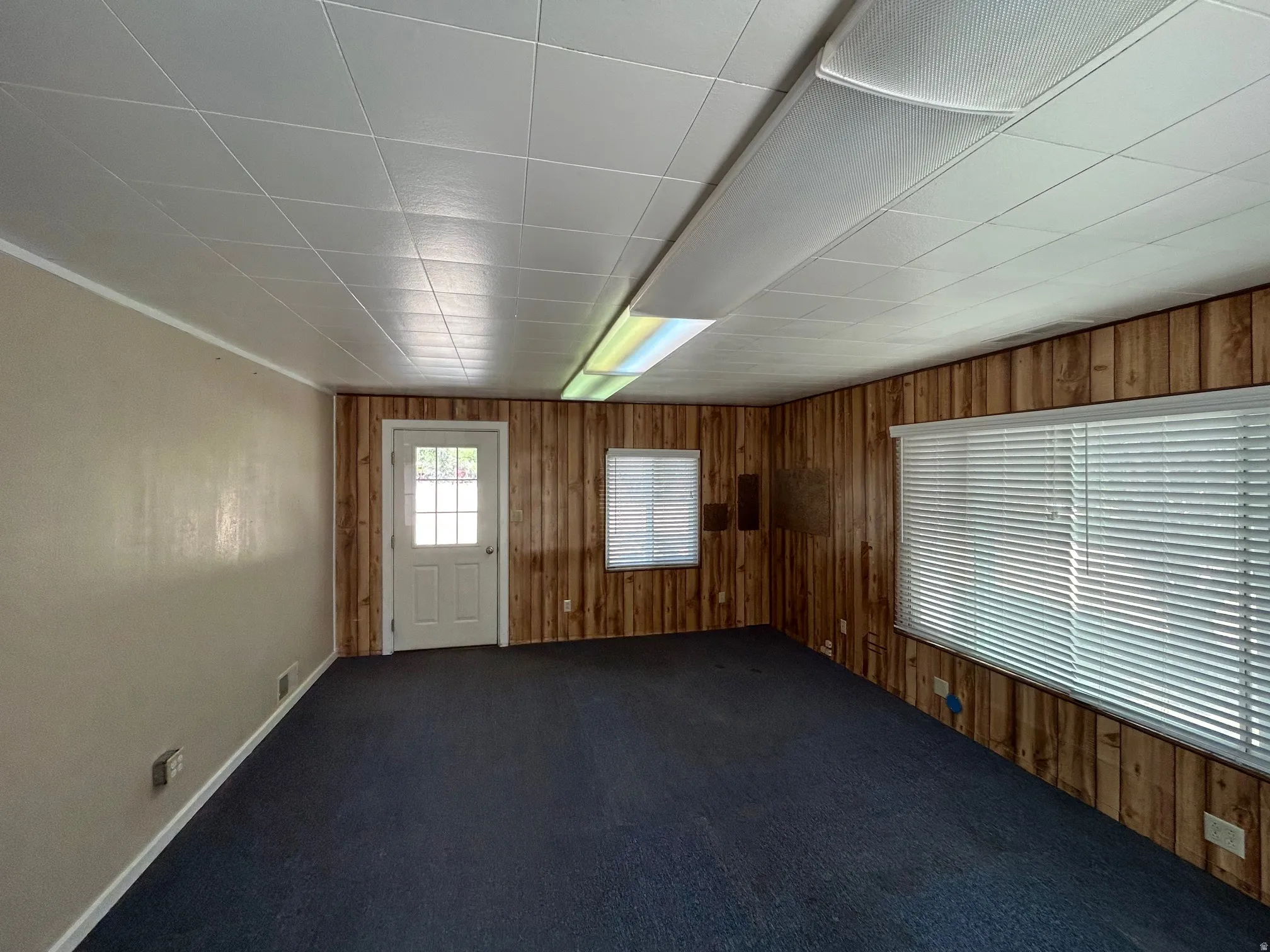 Interior room featuring paneled walls, a single window with blinds, and white door with window panes