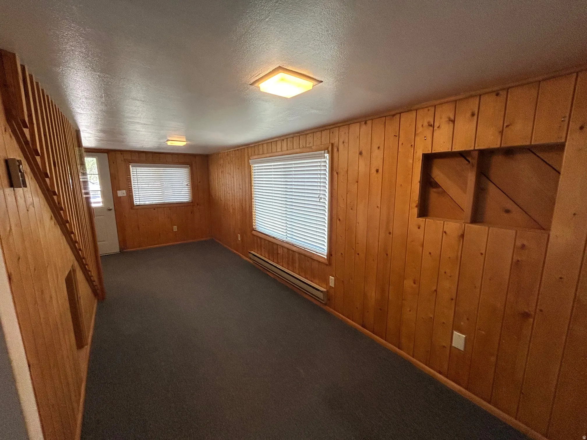 Interior space featuring wood paneling throughout, dark carpeting, and a white entry door