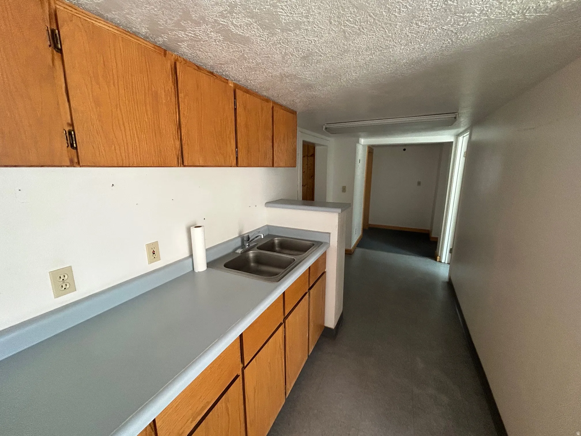 Kitchenette featuring wood-finish cabinetry, a double basin stainless steel sink, and light blue laminate countertops
