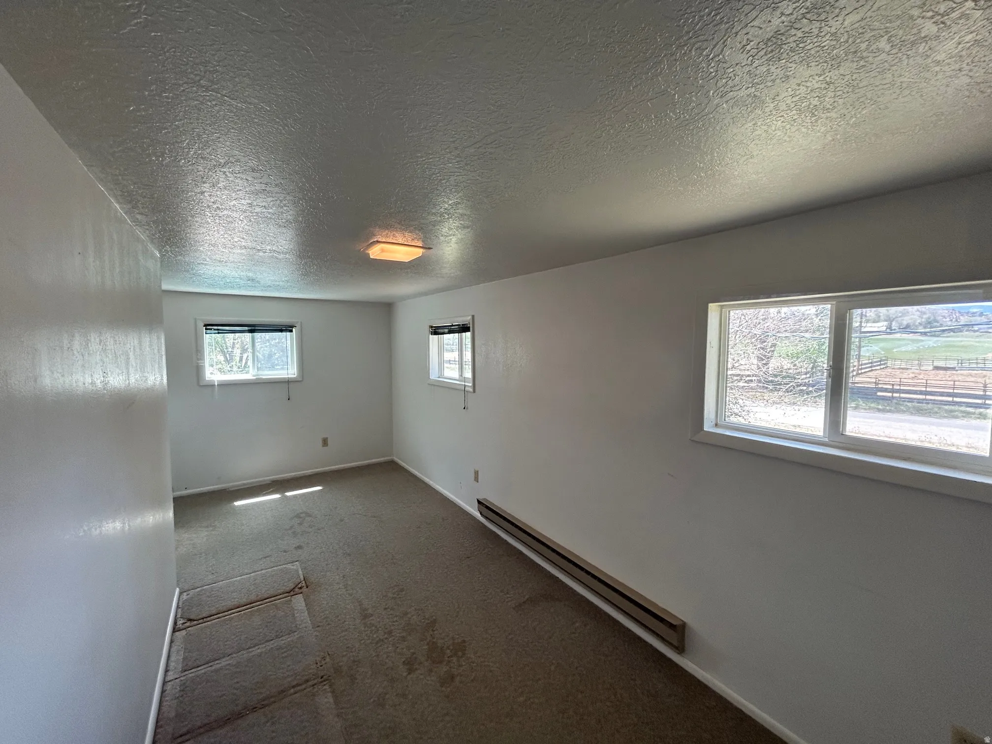 Carpeted interior room with white walls, a textured ceiling, and a flush-mount ceiling light fixture