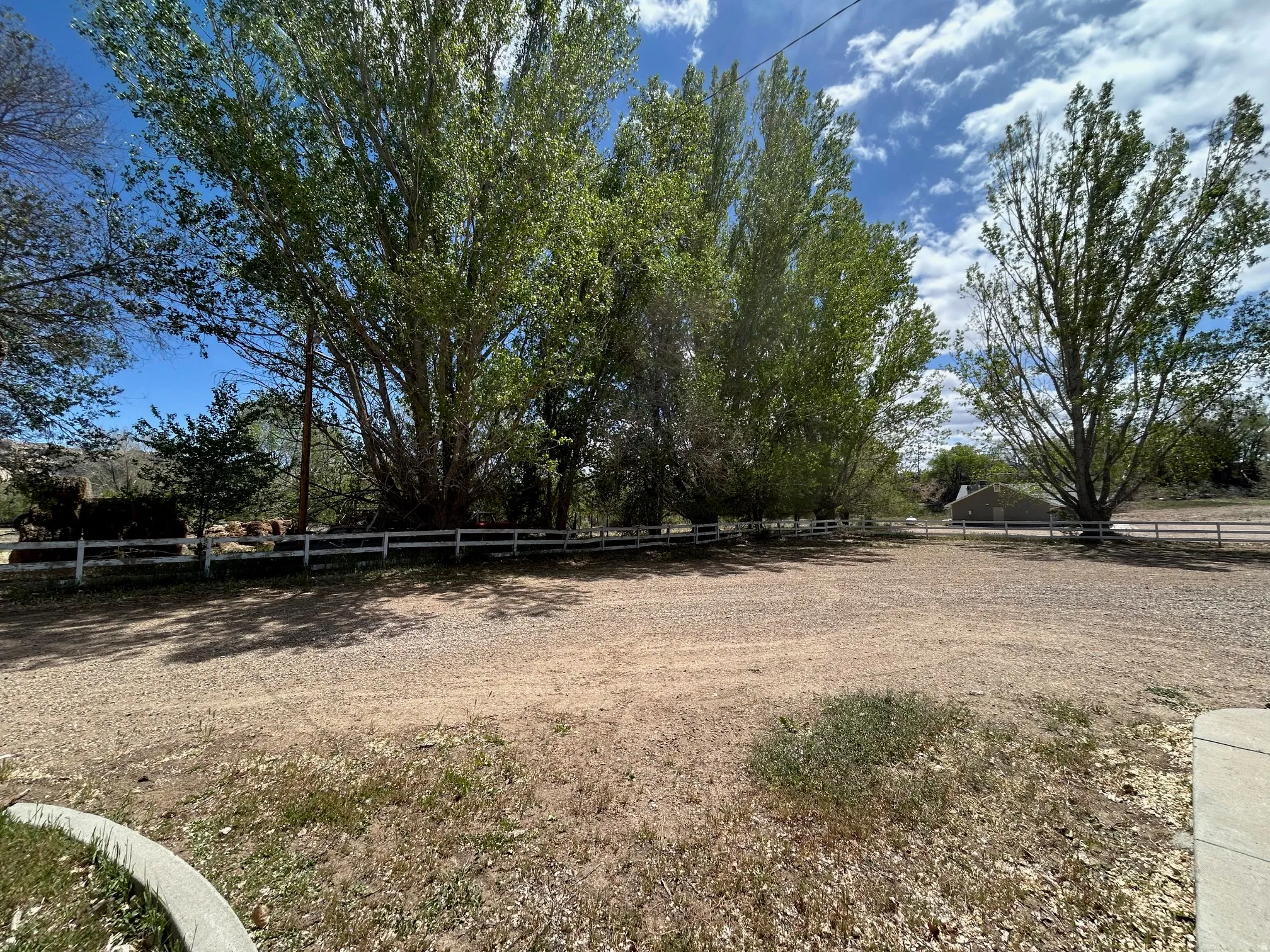 Expansive gravel lot with mature trees and a white split rail fence