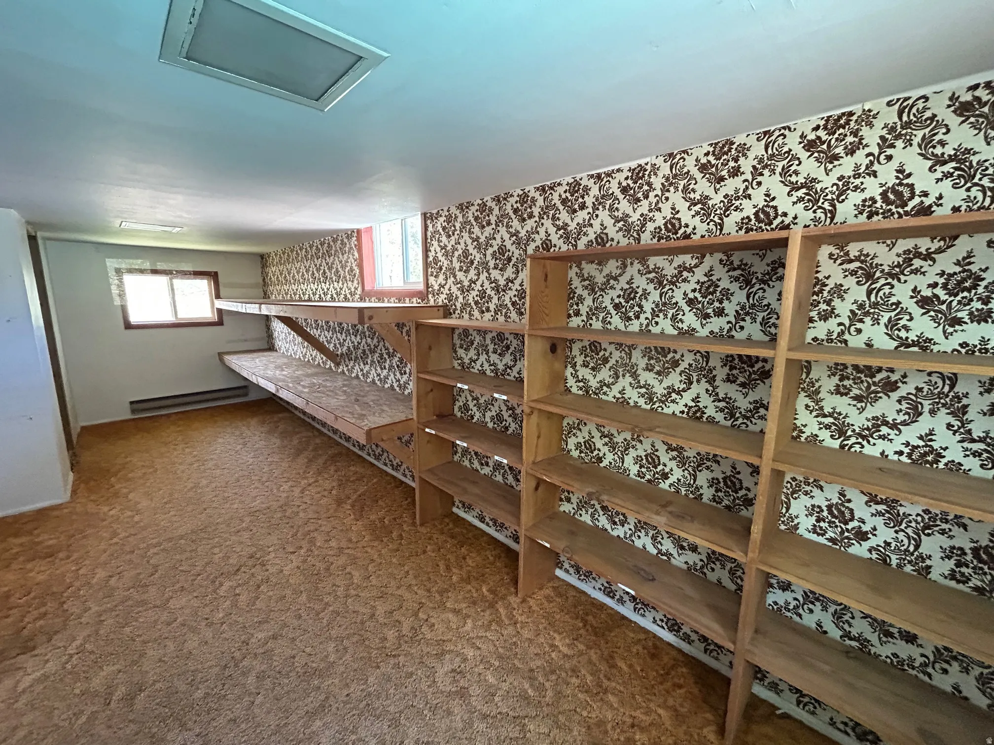 Room featuring built-in wooden shelving, patterned wallpaper, and a carpeted floor